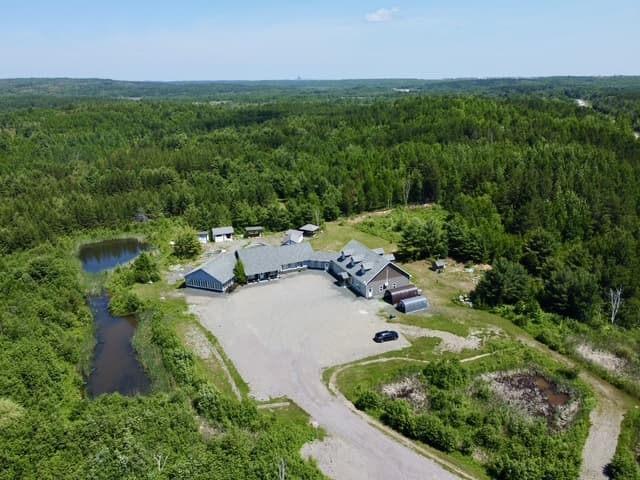Wide aerial view of the property, pond, and surrounding forest